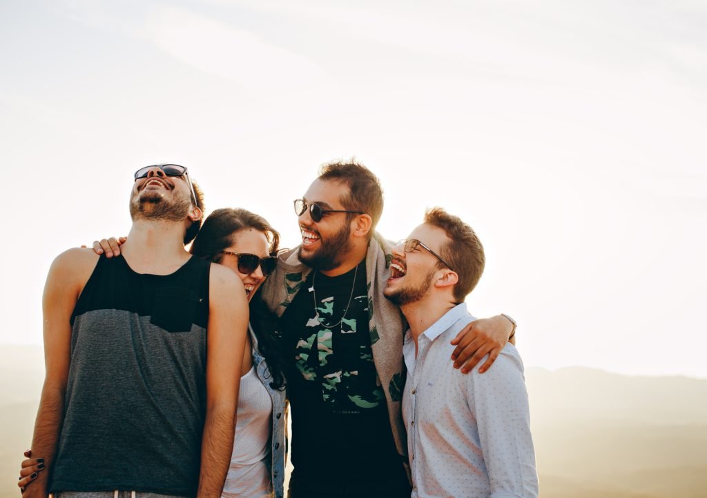 Four adults laughing together outdoors.